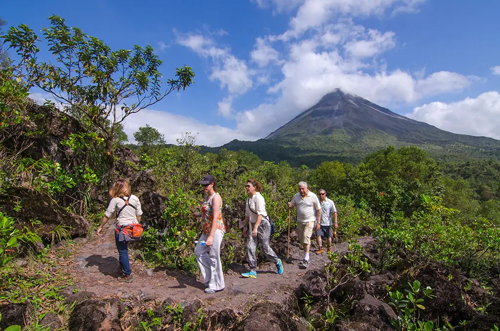 Grupo de visitantes en una caminata guiada con el cono del Volcán Arenal despejado al fondo